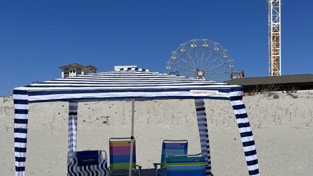 Ein Strandsonnenschirm mit Streifenmuster, zwei farbenfrohe Liegestühle und ein Riesenrad im Hintergrund.