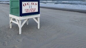 Ein Rettungsschwimmerstand mit einem Schild, auf dem steht: "AUF IHRE KINDER ACHTEN" und "O.C.B.P 11 IM ZWISCHEN DEN GRÜNEN BOJEN SCHWIMMEN".