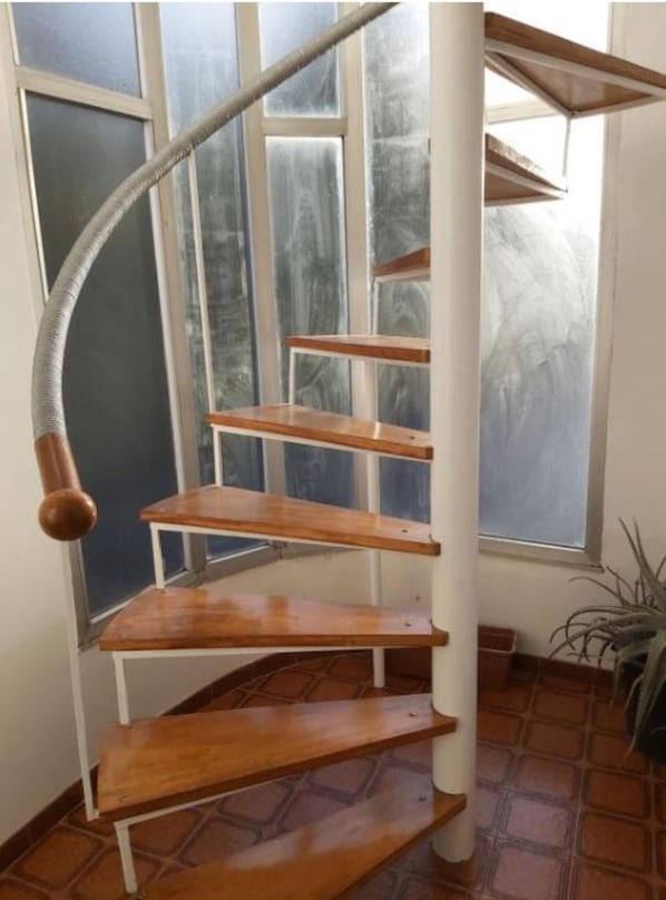Escadaria em espiral com degraus de madeira e corrimão de metal.
