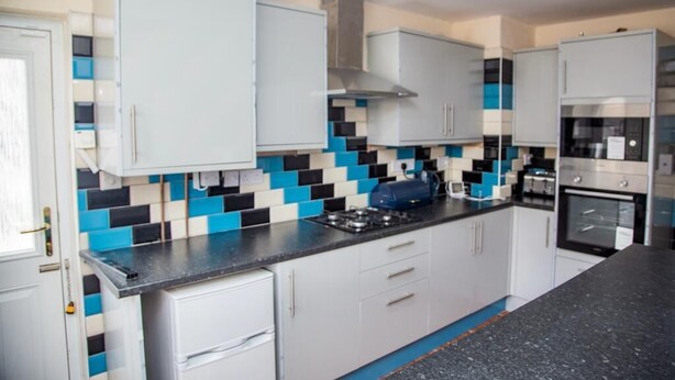 Cocina moderna con armarios blancos, encimera negra y salpicadero de azulejos azules y negros.