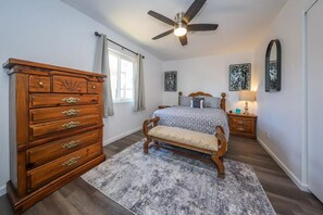 Un dormitorio con cómoda de madera, cama con banco, ventilador de techo y obras de arte en las paredes.