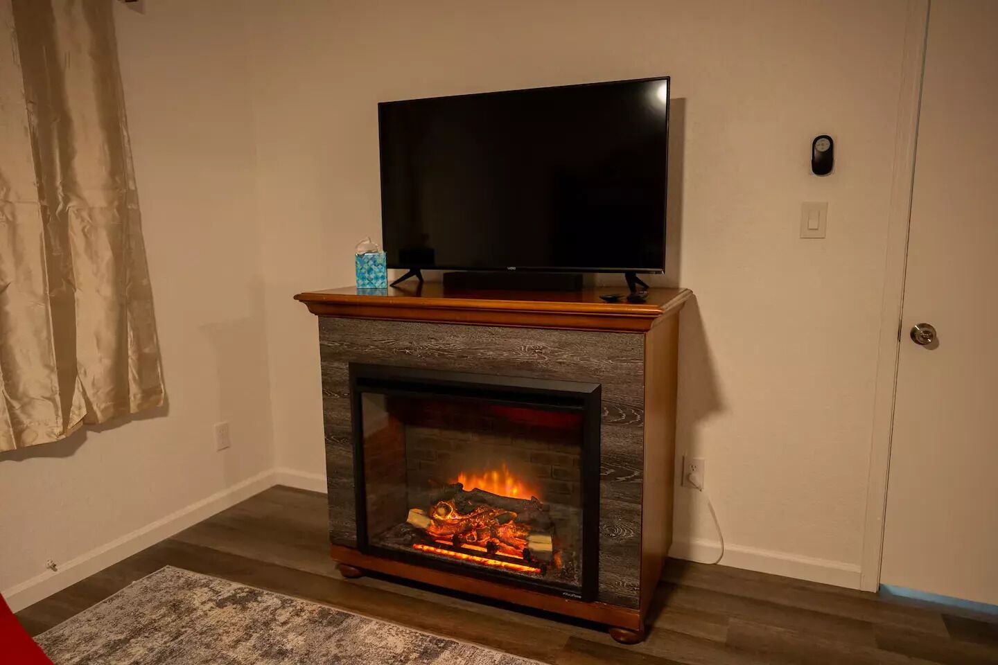 Sala de estar com lareira, televisão sobre um suporte de madeira e uma porta à direita.