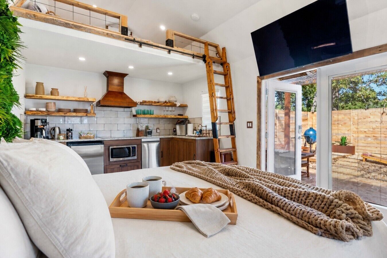 A modern kitchen with a lofted dining area, a wooden ladder, and a breakfast tray with croissants and berries.