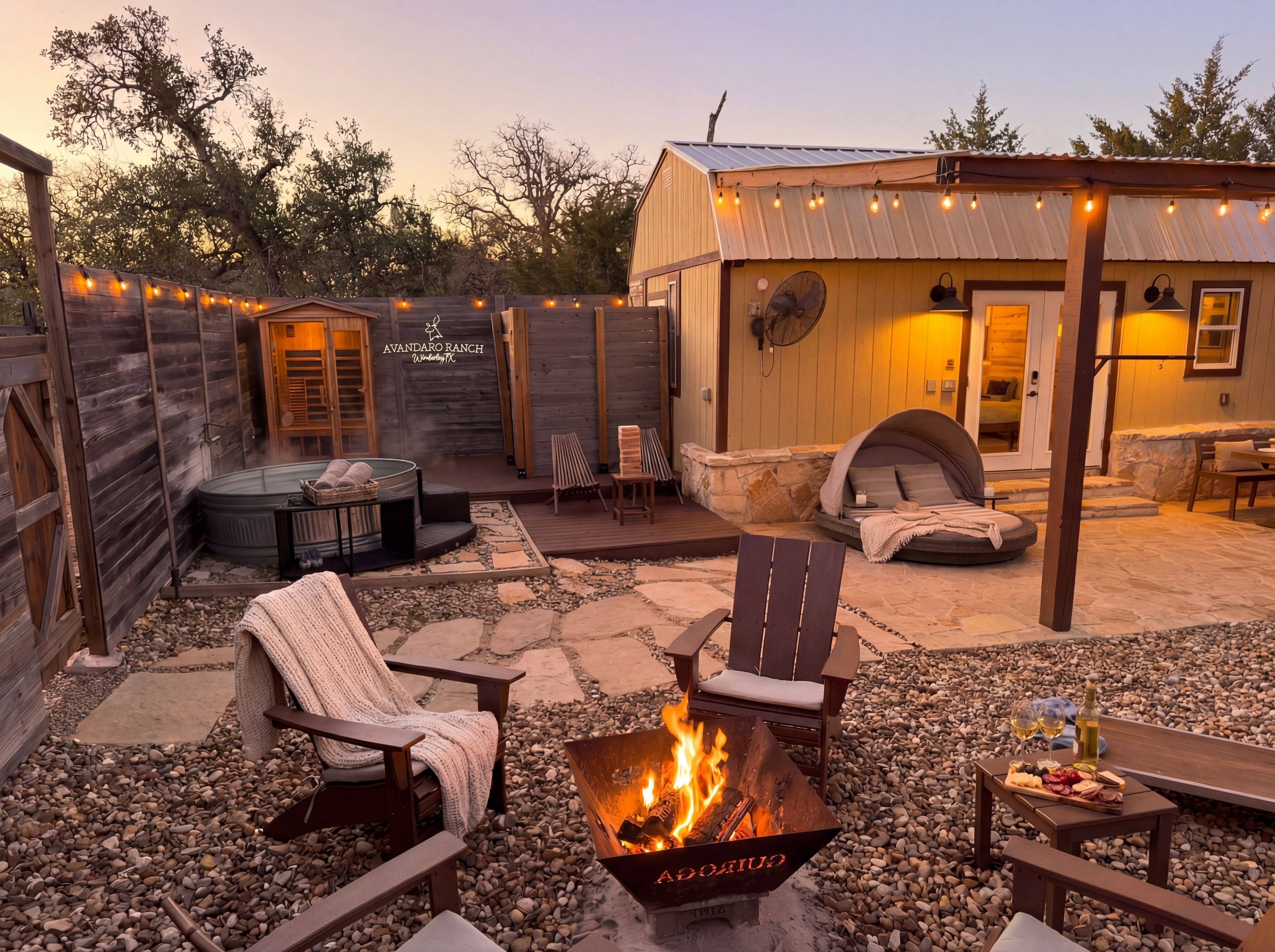 A cozy outdoor patio with a fire pit, seating, and a small building with a sign reading 'AVANDARO RANCH.'
