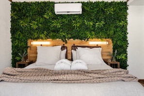 A bed with a headboard covered in green foliage, two bedside tables with lamps, and a knitted throw blanket. - A+ Privacy | Romantic Lux | Sauna | Hot/Cold Pool (Wimberley)