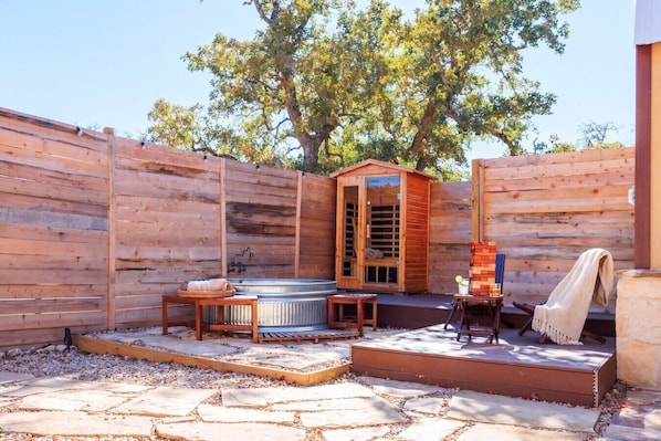 Una terraza de madera con un jacuzzi, una sauna de madera y una chimenea de piedra.