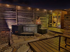 An outdoor sauna area with a hot tub, seating, and a wooden deck. - A+ Privacy | Romantic Lux | Sauna | Hot/Cold Pool (Wimberley)