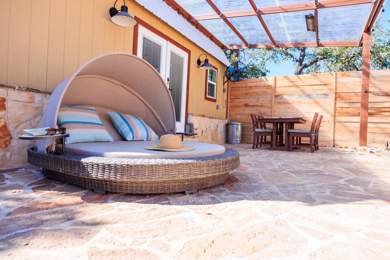Ein gemütlicher Sitzbereich im Freien mit einer gewölbten Rattan-Couch, einem Esstisch mit Stühlen und einer Pergola darüber.