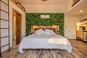 Un dormitorio con cama, cabecera de madera, pared verde y una zona de cocina.