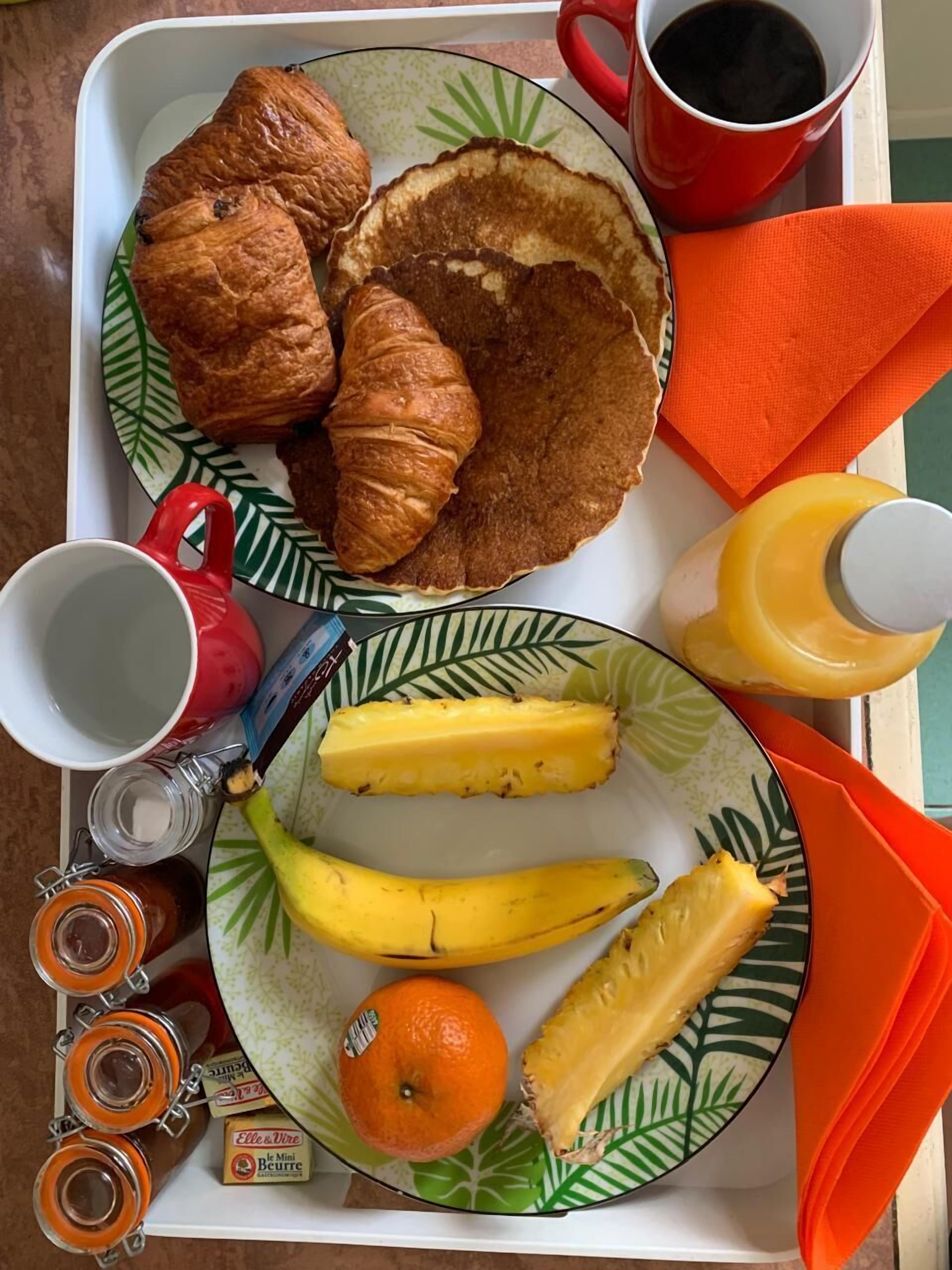 A tray with croissants, pancakes, a banana, an orange, and a pineapple.