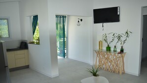 Een moderne keuken met een inbouwoven, een eethoek met een glazen tafel en stoelen, en een zithoek met een aan de muur bevestigde televisie.