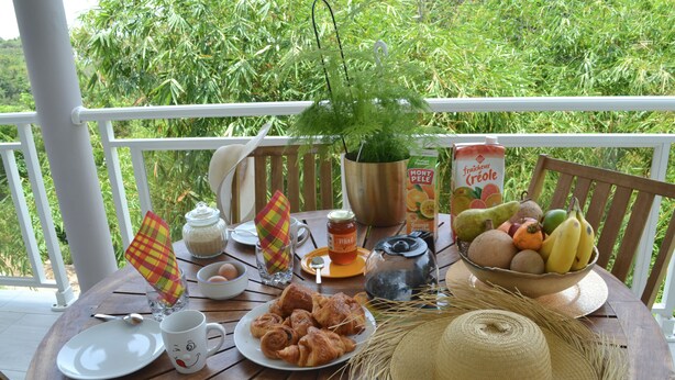 Een houten tafel gedekt met ontbijtartikelen, zoals croissants, een fruitschaal, een fles sap en een koffiepot.