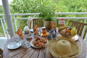 Ein Holztisch, reichhaltig gedeckt mit Frühstücksleckereien, darunter Croissants, eine Obstschale, Saft und eine Kaffeekanne.