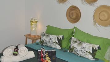 Ein ordentlich bezogenes Bett mit grün-blauer Bettwäsche, ein kleiner Nachttisch mit Lampe und eine Wand, die mit gewebten Hüten dekoriert ist.