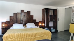 Un dormitorio moderno con cabecera de madera, colcha amarilla, dos lámparas de noche y un estante empotrado de madera con objetos decorativos.