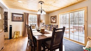 A dining area with a wooden table set for four, surrounded by chairs, with a view of a snowy deck outside. - 4-bedroom cabin just 10 minutes from Adirondack Park (Thendara)