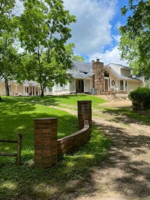 Une maison à deux étages, dotée d’une cheminée en pierre, d’un porche couvert et d’une pelouse bien entretenue.