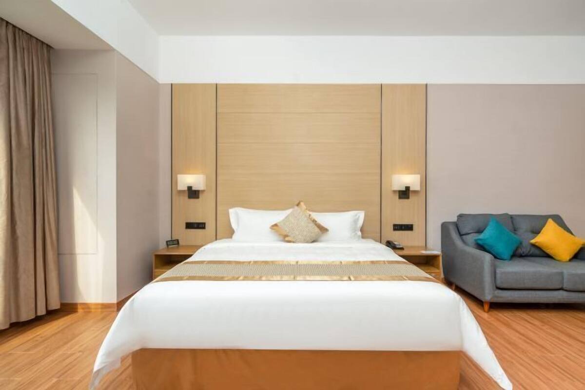 A hotel room with a large bed, a grey sofa, and two bedside lamps.