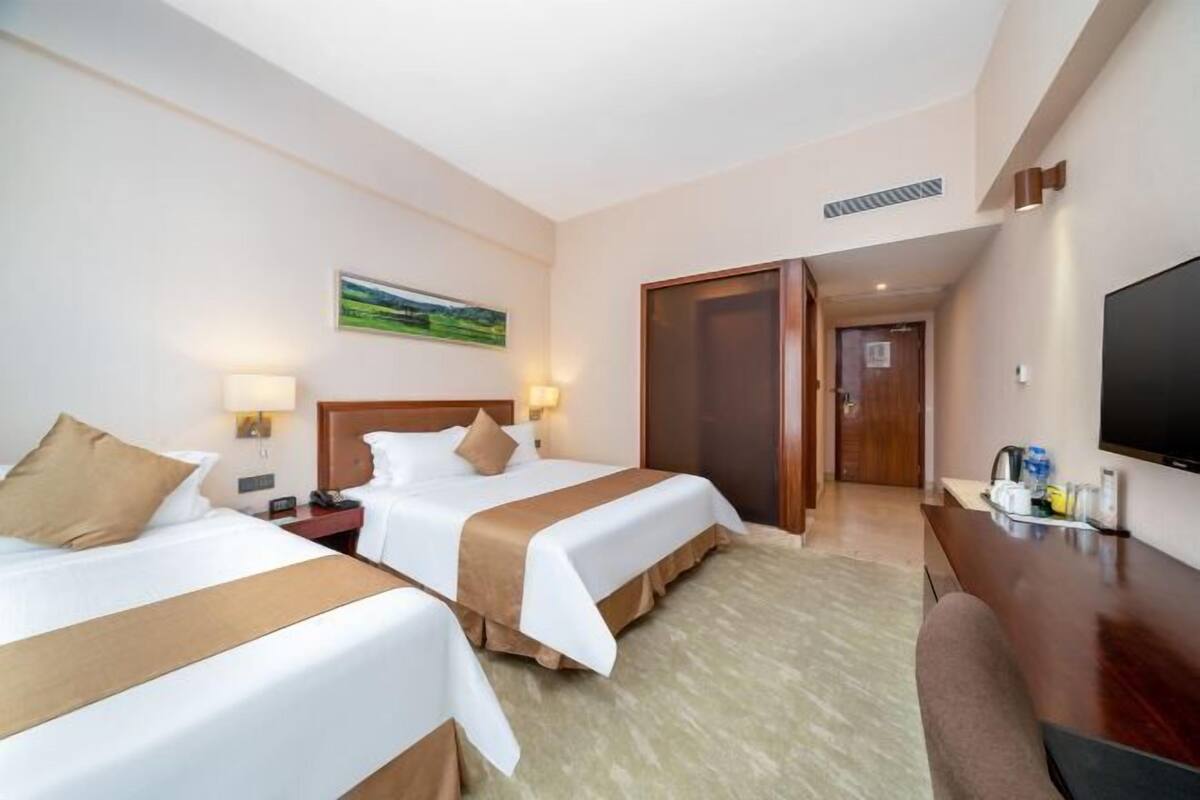 A hotel room with two beds, a desk, a TV, and a painting on the wall.