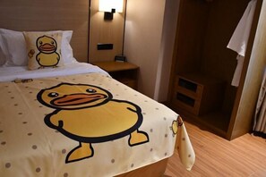 A hotel room with a bed featuring a duck-themed duvet cover, a bedside table with a lamp, and a wooden floor.