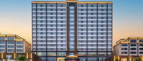 A multi-story hotel with a central entrance, surrounded by smaller buildings, and a clear sky.