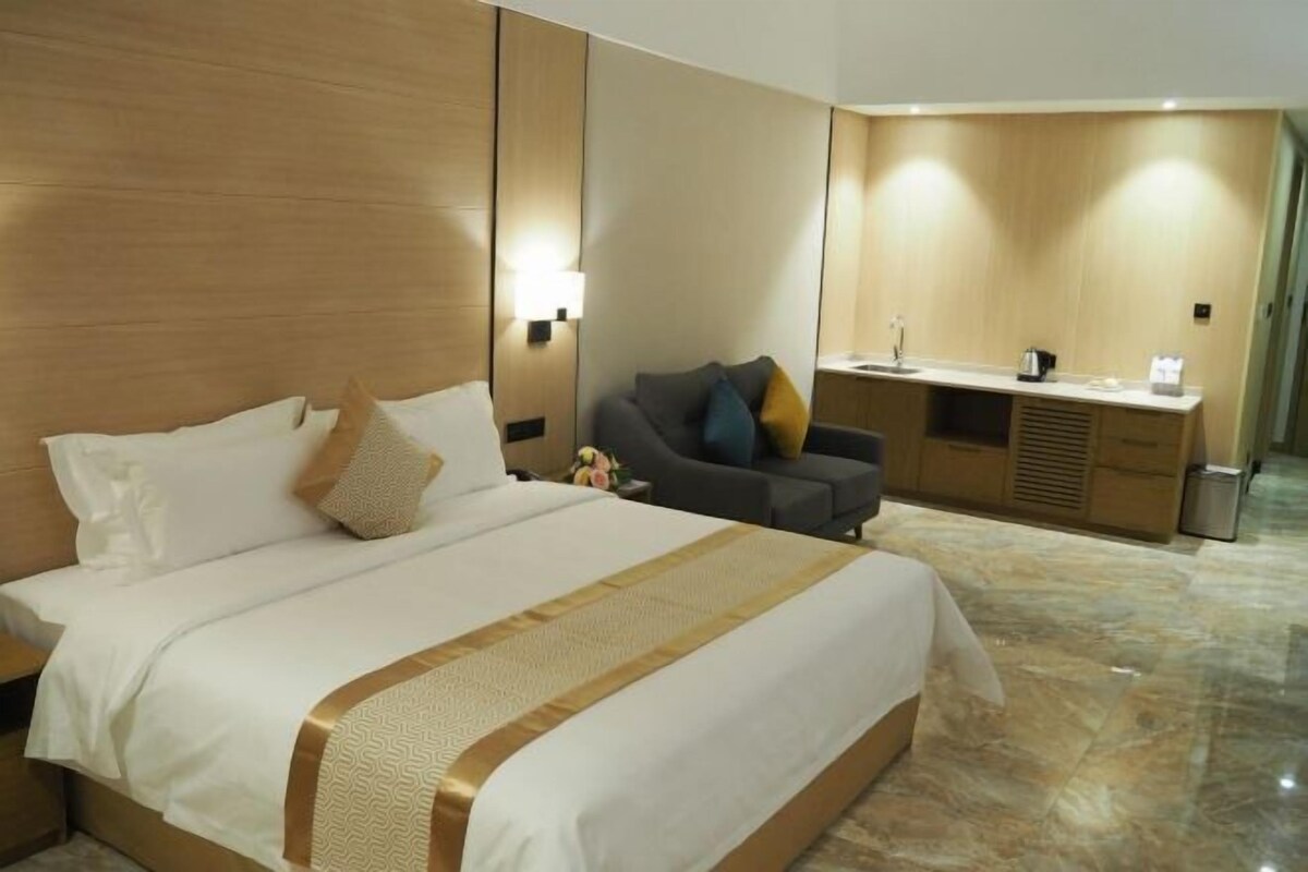 A hotel room with a large bed, a sofa, a desk, and a mirror.
