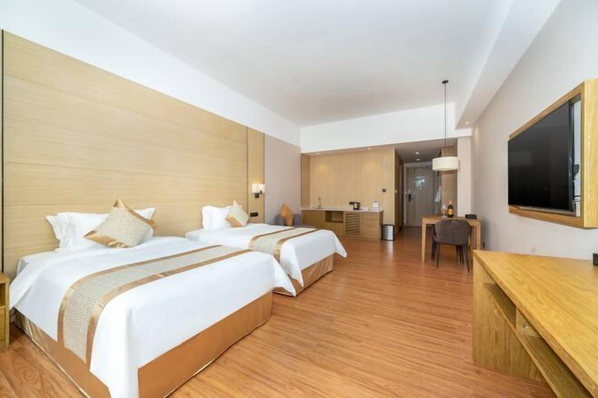 A hotel room with two beds, a desk, a chair, and a TV.