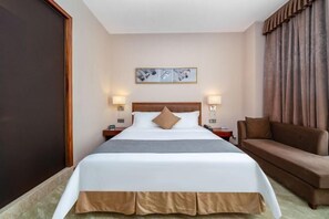 A hotel room with a large bed, a brown sofa, a painting on the wall, and two bedside lamps.
