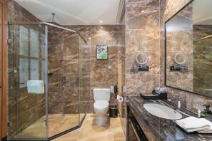 A modern bathroom with a glass-enclosed shower, a marble-tiled wall, a toilet, a sink, and a large mirror.