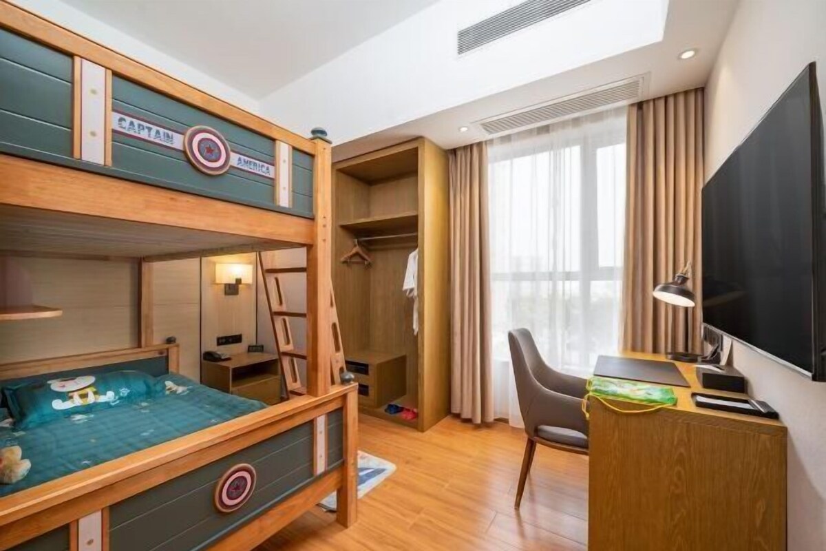A hotel room with a bunk bed, a desk with a chair, a TV, and a wardrobe.