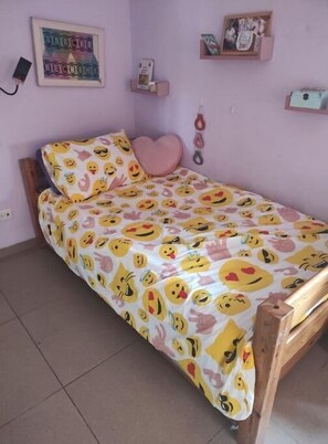 A bedroom with a bed covered in a colorful emoji print bedspread, a pink heart-shaped pillow, and a framed picture on the wall. - Large yet Cozy Home in Golan (Golan)