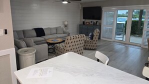 Ein modernes Wohnzimmer mit grauem Sofa, einem gemusterten Sessel und einem Esstisch mit einem Papier darauf.