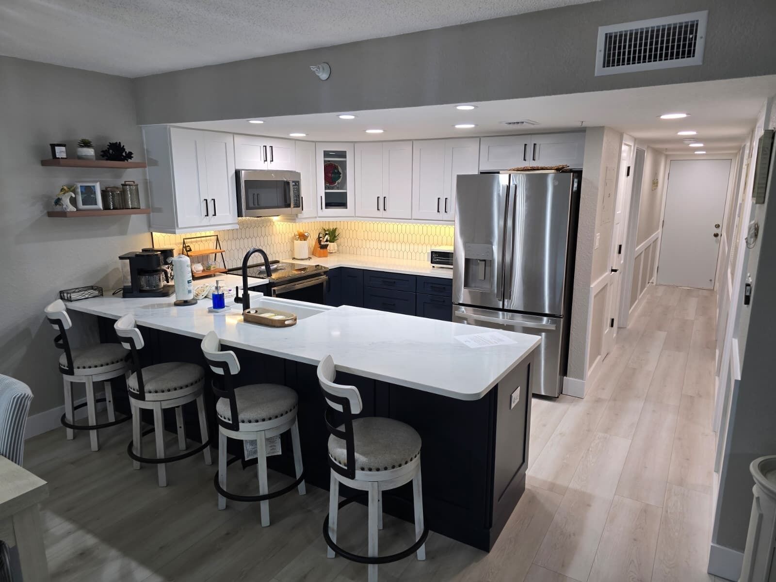 Une cuisine moderne avec des meubles blancs, des appareils en acier inoxydable et un îlot central doté de tabourets de bar.