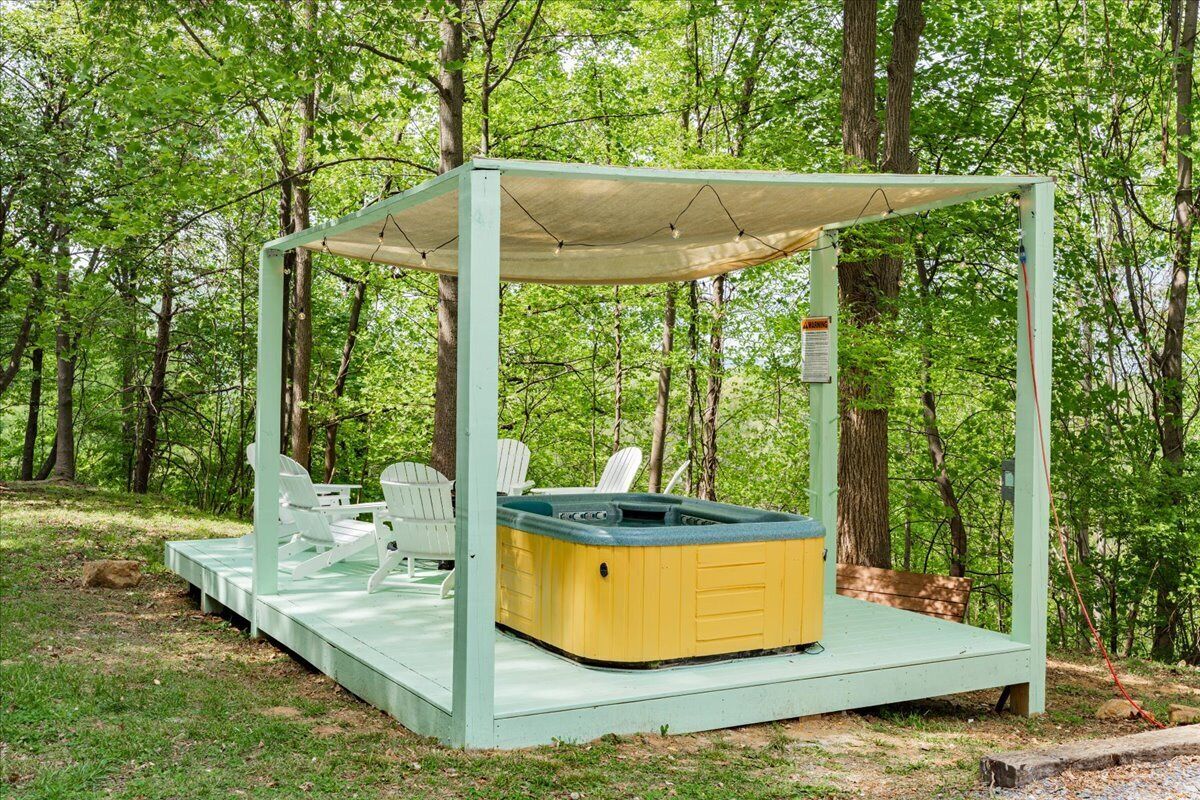 A hot tub on a wooden deck surrounded by Adirondack chairs in a wooded area.