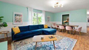Een woonkamer met een blauwe modulaire bank, een houten salontafel en een eetgedeelte met roze stoelen.