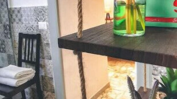 Ein Zimmer mit einem Holzstuhl, einem kleinen Tisch mit einer Topfpflanze und einer daran befestigten Kordel.