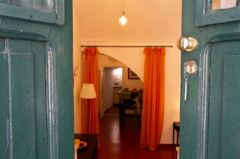 A doorway with a green door and orange curtains leading to a room with a lamp and a table.