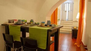 Un coin repas avec une table dressée pour quatre personnes, des chaises et une petite table avec une lampe.