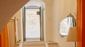 Un couloir avec un escalier menant à une porte, une petite table avec une bougie et une lampe fixée au mur.