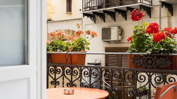 A balcony with a table and chairs, potted plants, and a window.