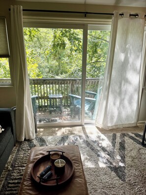 A room with a sliding glass door leading to a balcony with a wooden deck and a view of trees. - Walkable 2BR Sugar Mountain Boho Condo Retreat with Private Creekside Balcony (Sugar Mountain)