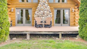 Une cabane en rondins avec une cheminée en pierre, de grandes fenêtres et une terrasse avec des chaises.