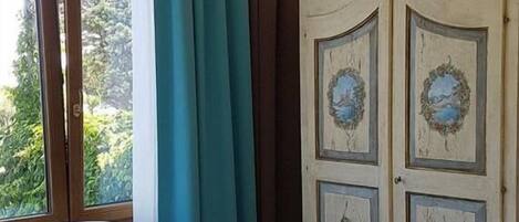 Una habitación con un sillón blanco, cortinas color aguamarina y un armario blanco con paneles decorativos.