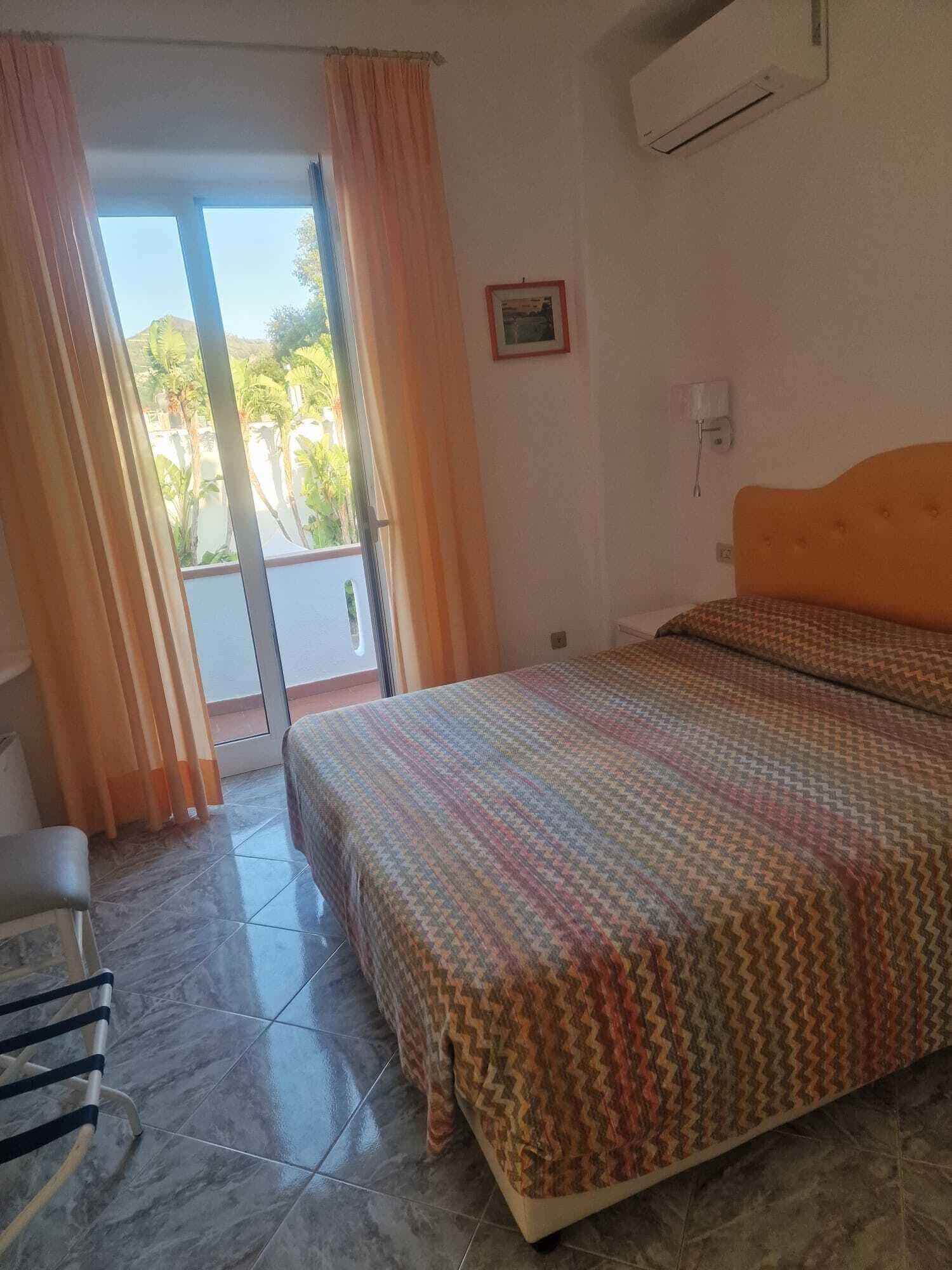 A room with a bed, a chair, a window with curtains, and an air conditioning unit.
