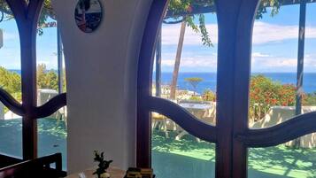 Ein Essbereich mit Tisch für zwei Personen, großen Bogenfenstern und Blick auf das Meer und die grüne Landschaft.