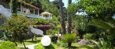 A lush garden with a white gazebo, palm trees, and a variety of plants.