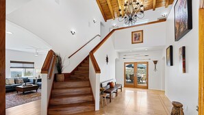 A spacious living area with a wooden staircase, a chandelier, and a large window. - Mountaintop Ramona Home: Private Pool, Near Lake! (Ramona)