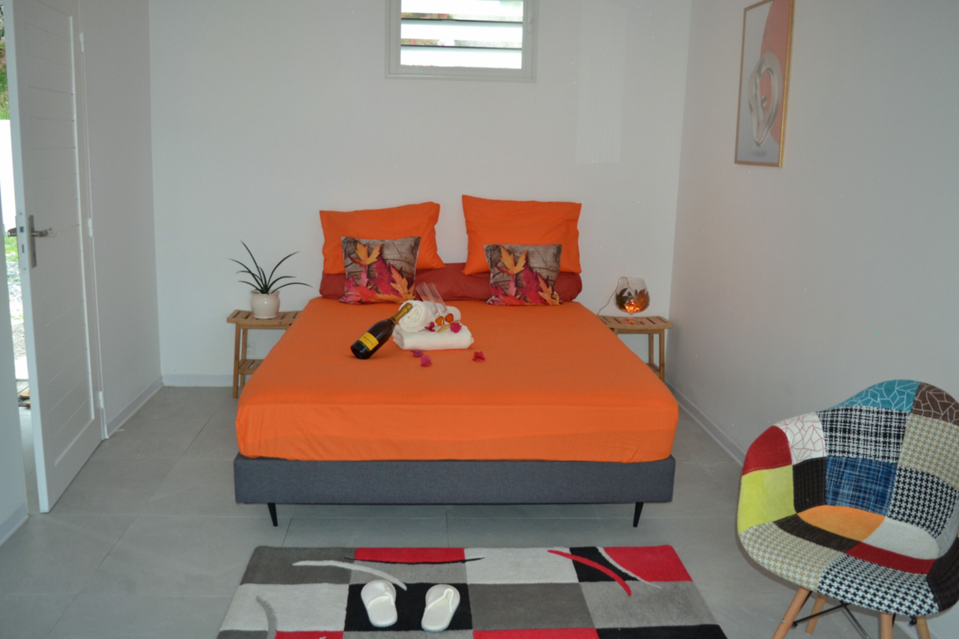 Un dormitorio con cama, almohadas, una botella, una planta y una silla.
