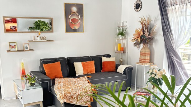 A modern living room with a sectional sofa, a side table, a mirror, a framed artwork, and a potted plant. - Logement "paprika" 2 À 6 Pers (Le Gosier)