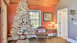 Un albero di Natale in una stanza con una poltrona a quadri, una lampada e un quadro appeso al muro.